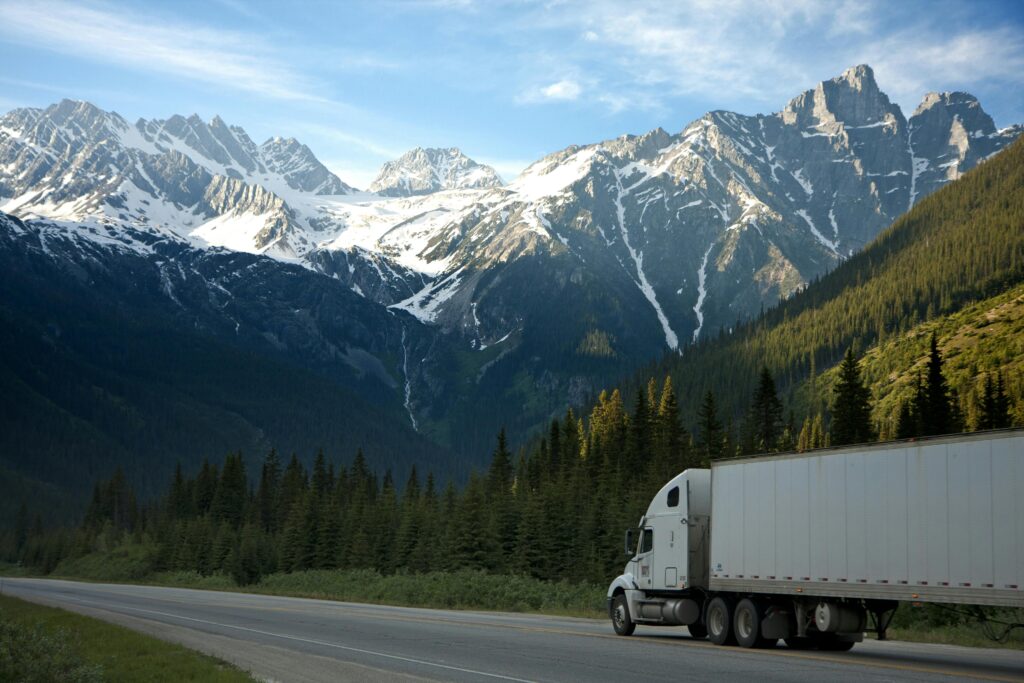 pexels-photo-93398-93398 A semi-truck travels along a highway with snow-capped mountains in the background.